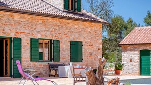 A stone building with green shutters, a patio with a table and chairs, and a pink lounge chair. - Stunning Renovated Traditional Stone Villa, Private Pool & Mountain Views just 800 m from the Sea! (Stari Grad)