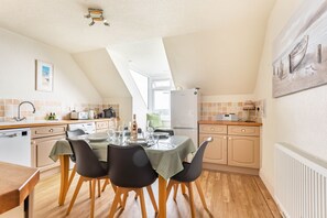 A kitchen with a dining table set for four, a refrigerator, and a window providing natural light. - Bessborough Green - Two Bedroom Apartment, Sleeps 4 (St Mawes)