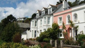 A row of white and pink buildings with multiple windows and a stone wall in the foreground. - Bessborough Green - Two Bedroom Apartment, Sleeps 4 (St Mawes)