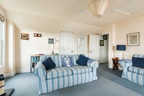 A living room with a striped sofa, a small table with a lamp, and a bookshelf. - Bessborough Green - Two Bedroom Apartment, Sleeps 4 (St Mawes)