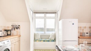 A compact kitchen with a built-in bench, a washing machine, and a refrigerator. - Bessborough Green - Two Bedroom Apartment, Sleeps 4 (St Mawes)