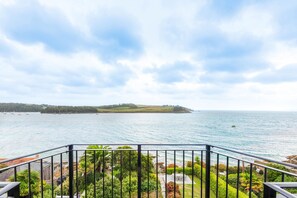 A balcony with a view of the sea, a grassy area with plants, and a distant hill. - Bessborough Green - Two Bedroom Apartment, Sleeps 4 (St Mawes)
