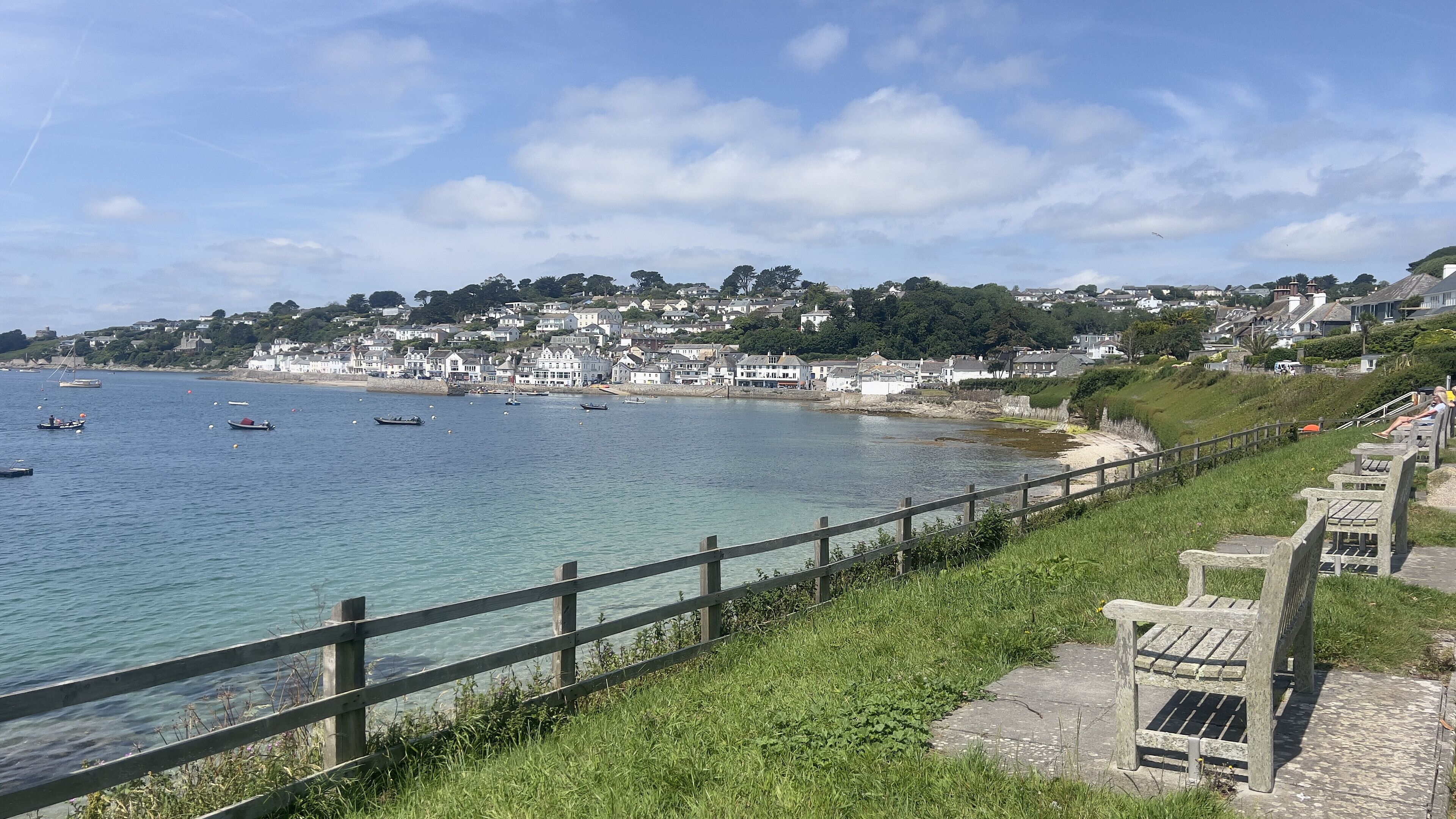 A coastal town with a wooden promenade overlooking the sea, houses along the hillside, and boats in the water.
