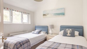 A bedroom with two beds, a window with a view of the beach, and a painting of the beach on the wall. - Bessborough Green - Two Bedroom Apartment, Sleeps 4 (St Mawes)