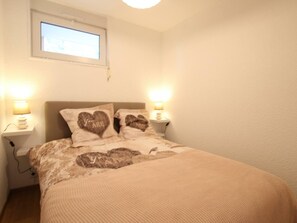 Quarto com uma cama, duas luminárias de cabeceira, uma janela e um ponto de luz na parede.