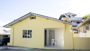 A yellow single-story house with a tiled roof, a small porch with two white plastic chairs, and a satellite dish on the roof. - Casa 2 Amarela - Casa piscina 10 pessoas (Itapema)