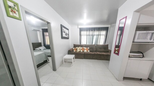 A compact living space with a bed, a sofa, a small table, and a mirror. - Casa 2 Amarela - Casa piscina 10 pessoas (Itapema)