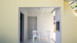 A hallway with a door, two white plastic chairs, and a small window with a stone-like texture. - Casa 2 Amarela - Casa piscina 10 pessoas (Itapema)