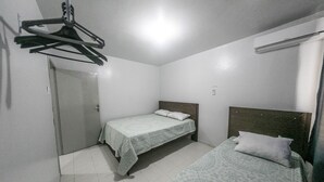 A small, clean room with two beds, a door, and a hanging clothes rack. - Casa 2 Amarela - Casa piscina 10 pessoas (Itapema)