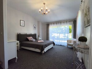 A bedroom with a bed, bedside table, lamp, chair, and a potted plant.