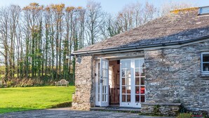 A stone building with a stone roof, a wooden bench, and a grassy area in the foreground. - Lamellyon Roundhouse (Lanteglos)