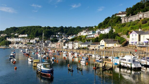 A harbor with numerous boats docked, surrounded by residential buildings and greenery. - Lamellyon Roundhouse (Lanteglos)