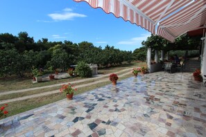 Un patio al aire libre con suelo de baldosas, plantas en macetas y un toldo a rayas.