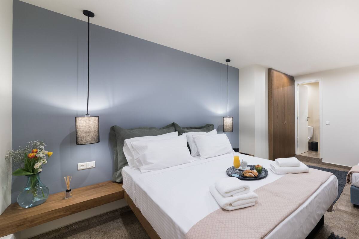 A modern hotel room with a large bed, a smaller bed, a bedside table with a vase of flowers, and a nightstand.