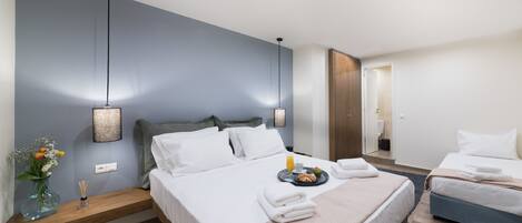 A modern hotel room with a large bed, a smaller bed, a bedside table with a vase of flowers, and a nightstand.