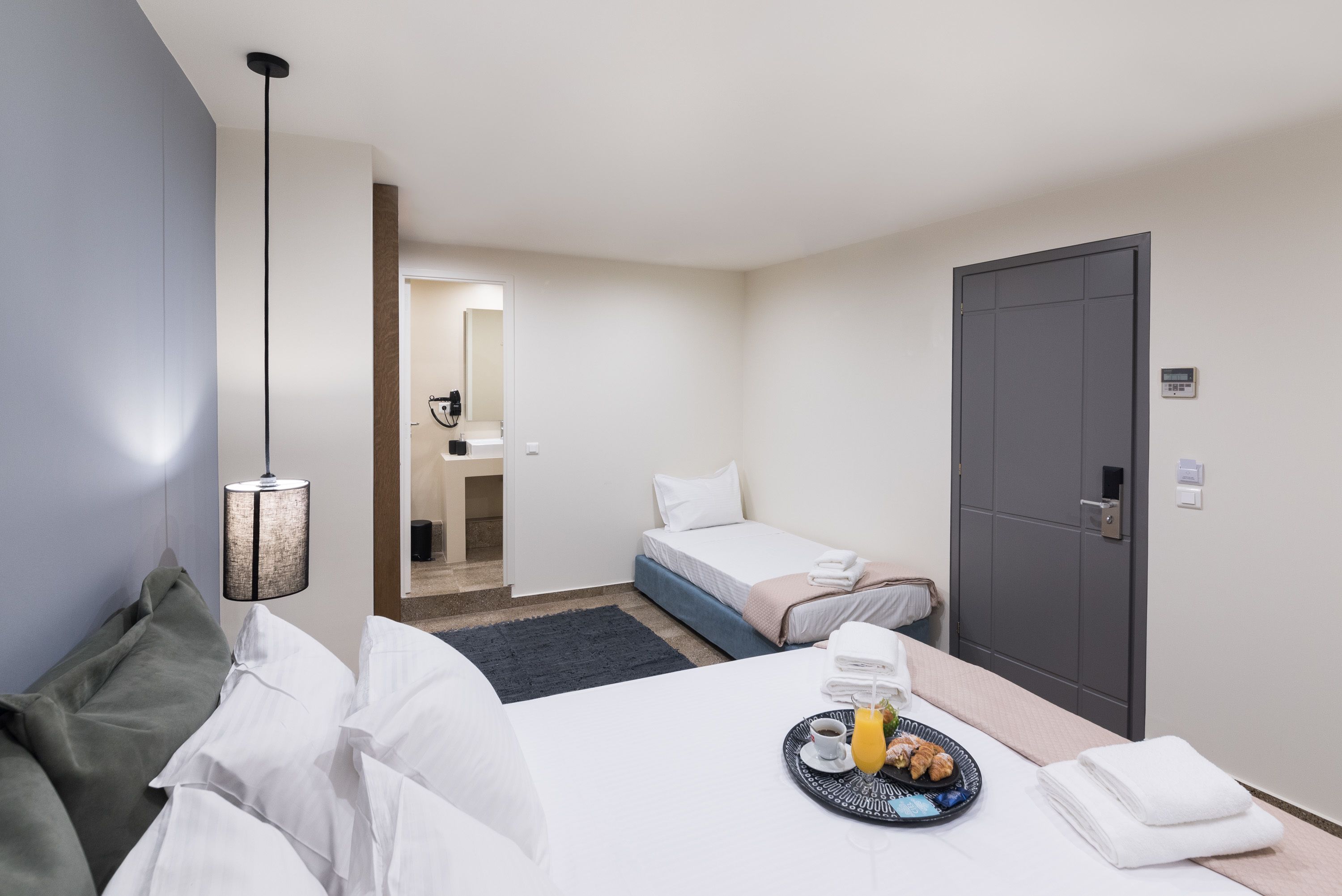 A hotel room with a bed, a bedside table with a tray of breakfast, a desk with a chair, a wardrobe, and a mirror.