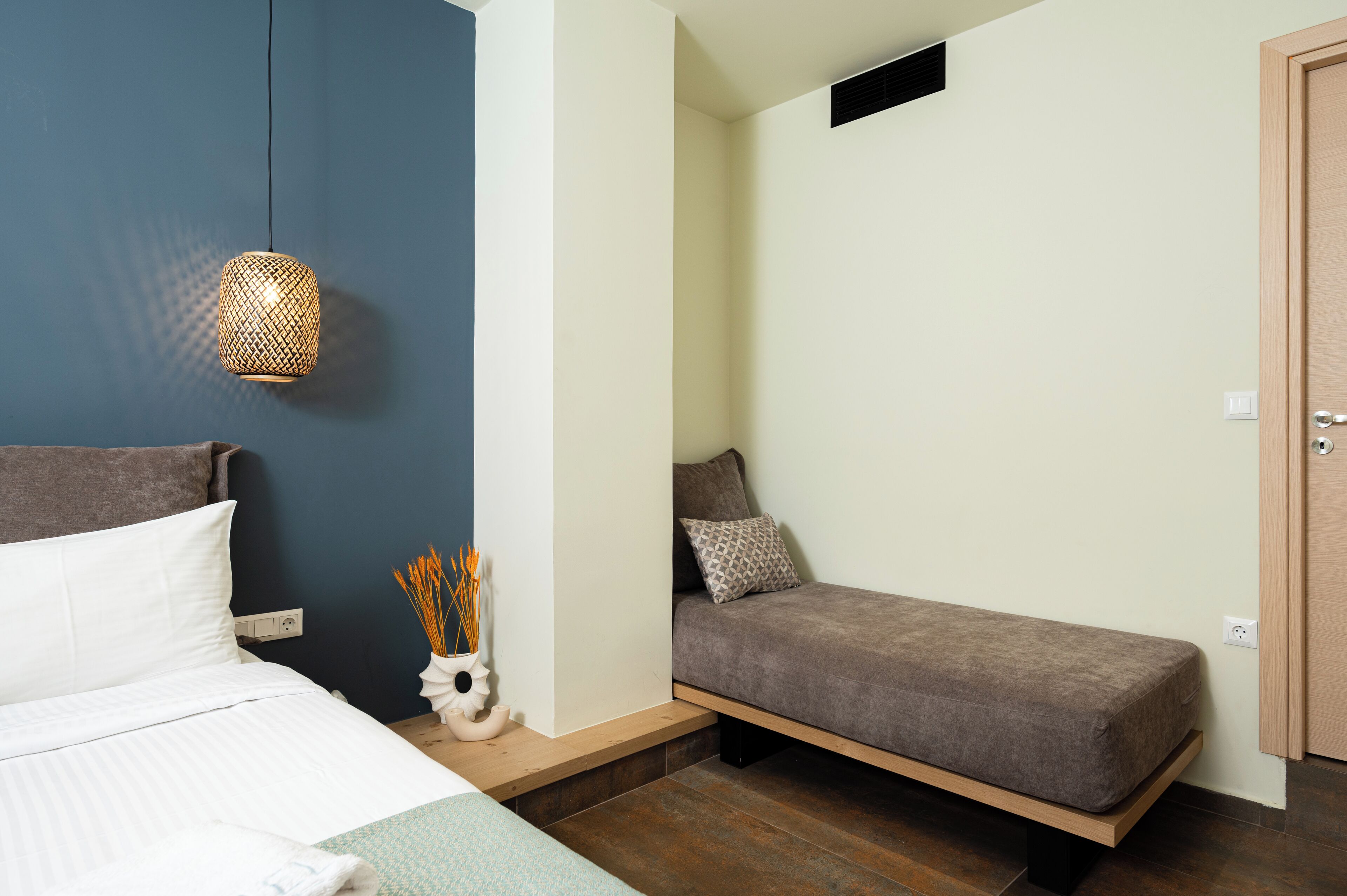 A bedroom with a bed, a bedside table with a decorative vase, a bench, and a hanging light fixture.