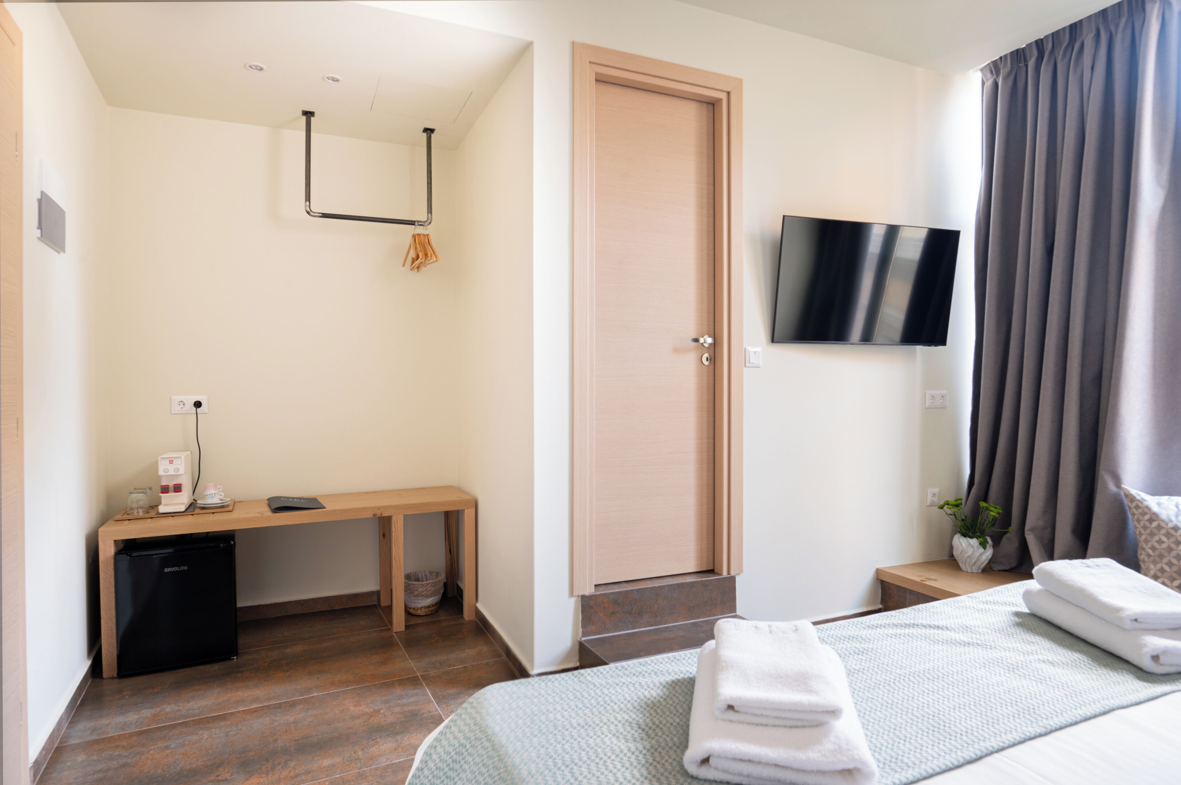 A hotel room with a bed, a desk with a coffee machine, a TV, and a door.