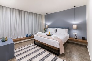 Una habitación de hotel moderna con una cama grande, una mesita de noche, una alfombra estampada y vistas al exterior.