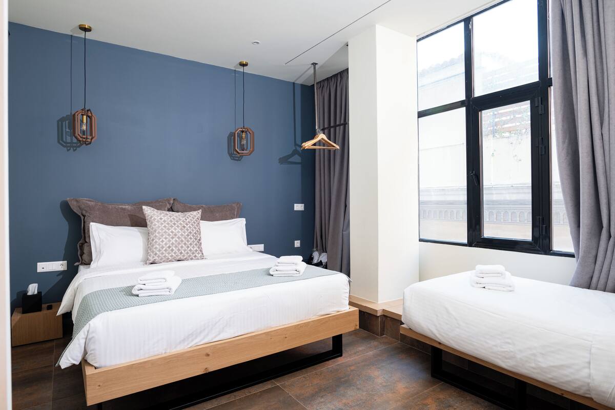 A hotel room with a large bed, a smaller bed, and a window with curtains.