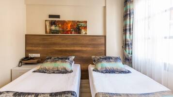 A hotel room with two single beds, a wooden headboard, a painting on the wall, a nightstand with a phone, and a window with curtains.