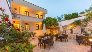 An outdoor patio with tables and chairs, surrounded by a stone wall and a building with multiple windows. - Old Town Boutique Hotel (Kusadasi)