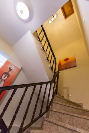 A grand staircase with a handrail and a painting above, set against a beautifully finished ceiling.