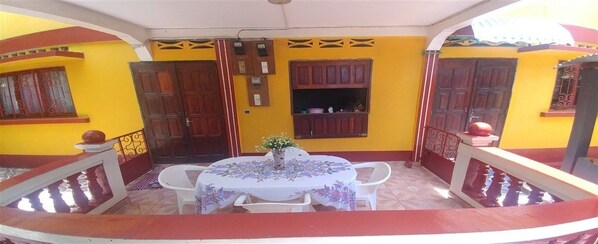 Un balcón con mesa y sillas, una planta en maceta y una puerta de madera.