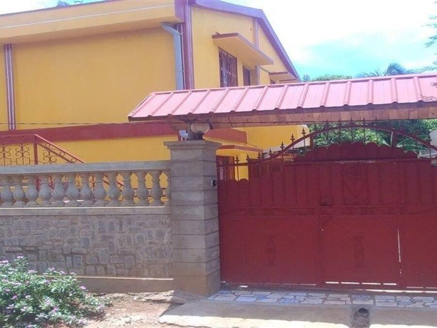 Un edificio amarillo con un portón rojo y una escalera que lleva a un balcón.