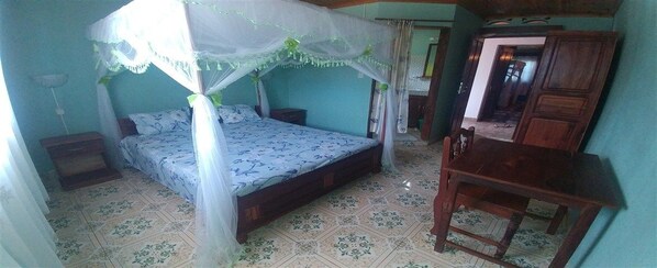 A bedroom with a bed under a canopy, a wooden nightstand, a wooden table, and a chair.