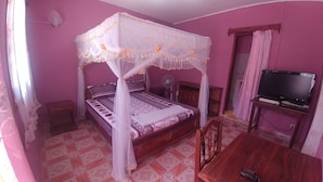Ein Schlafzimmer mit einem Himmelbett, einem Fernseher auf einem Holztisch und einem Wandventilator.