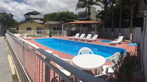 A swimming pool with lounge chairs and a table, surrounded by a fence and palm trees.