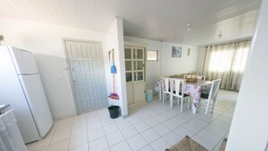 A kitchen with a refrigerator, a dining table with chairs, a broom, and a trash bin.