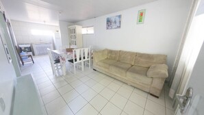 A living room with a beige sofa, a dining table with chairs, and a kitchen area in the background.