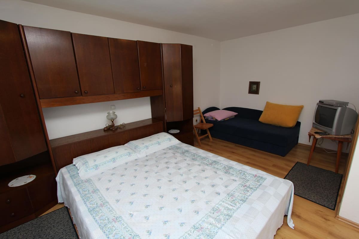 A bedroom with a bed, a small sofa, a television, and wooden cabinets.