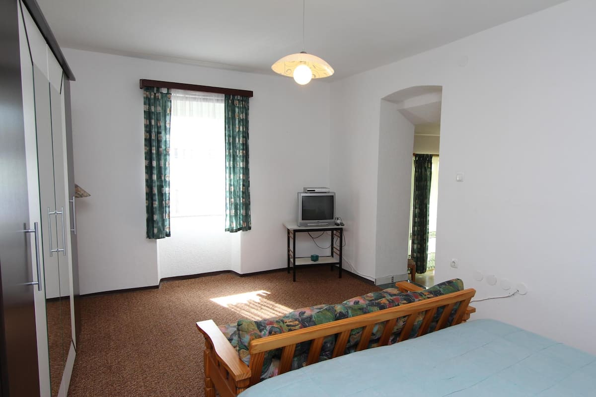 A bedroom with a bed, a television on a small table, and a window with curtains.