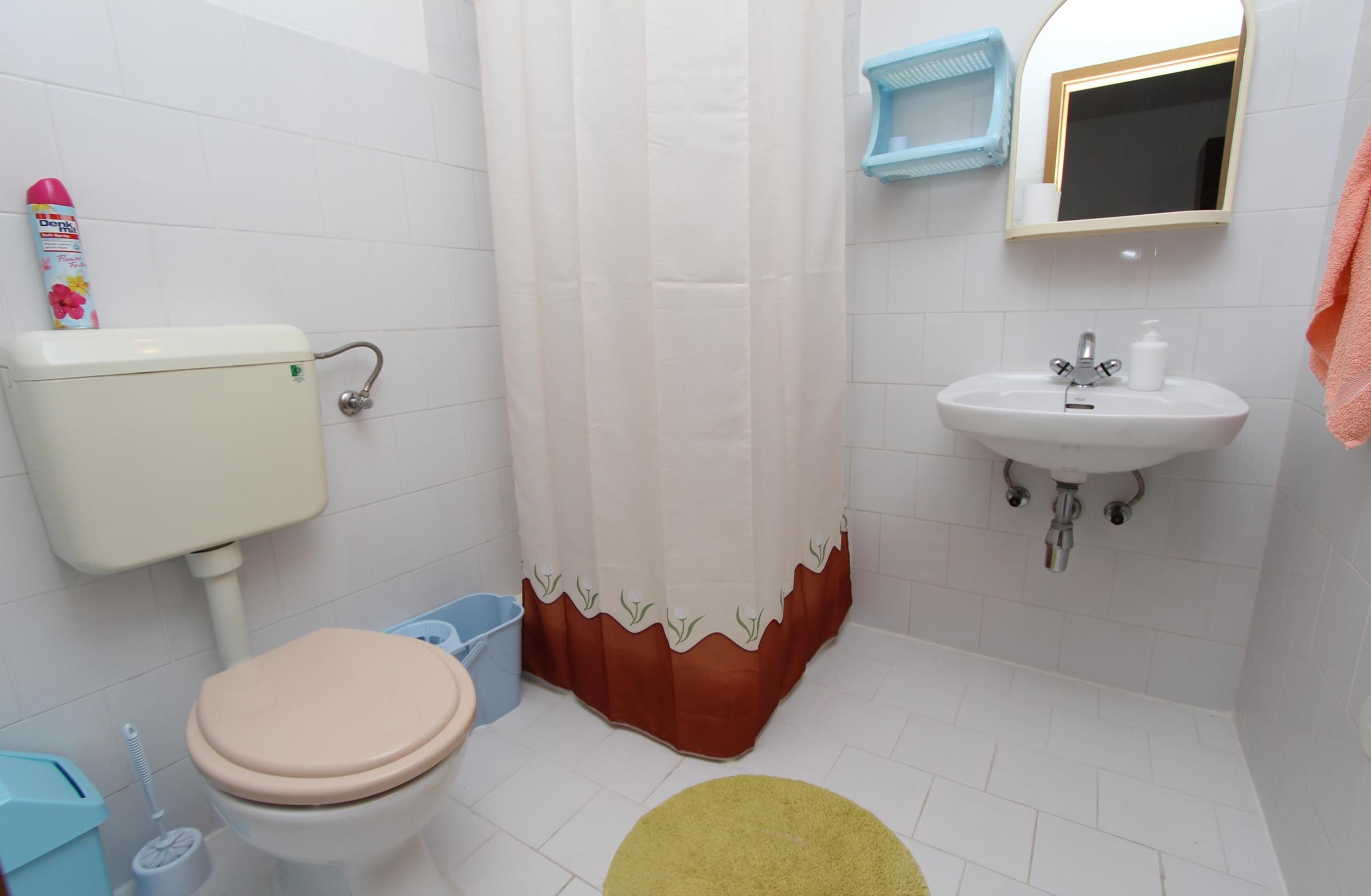 A bathroom with a toilet, sink, shower curtain, and a yellow rug.