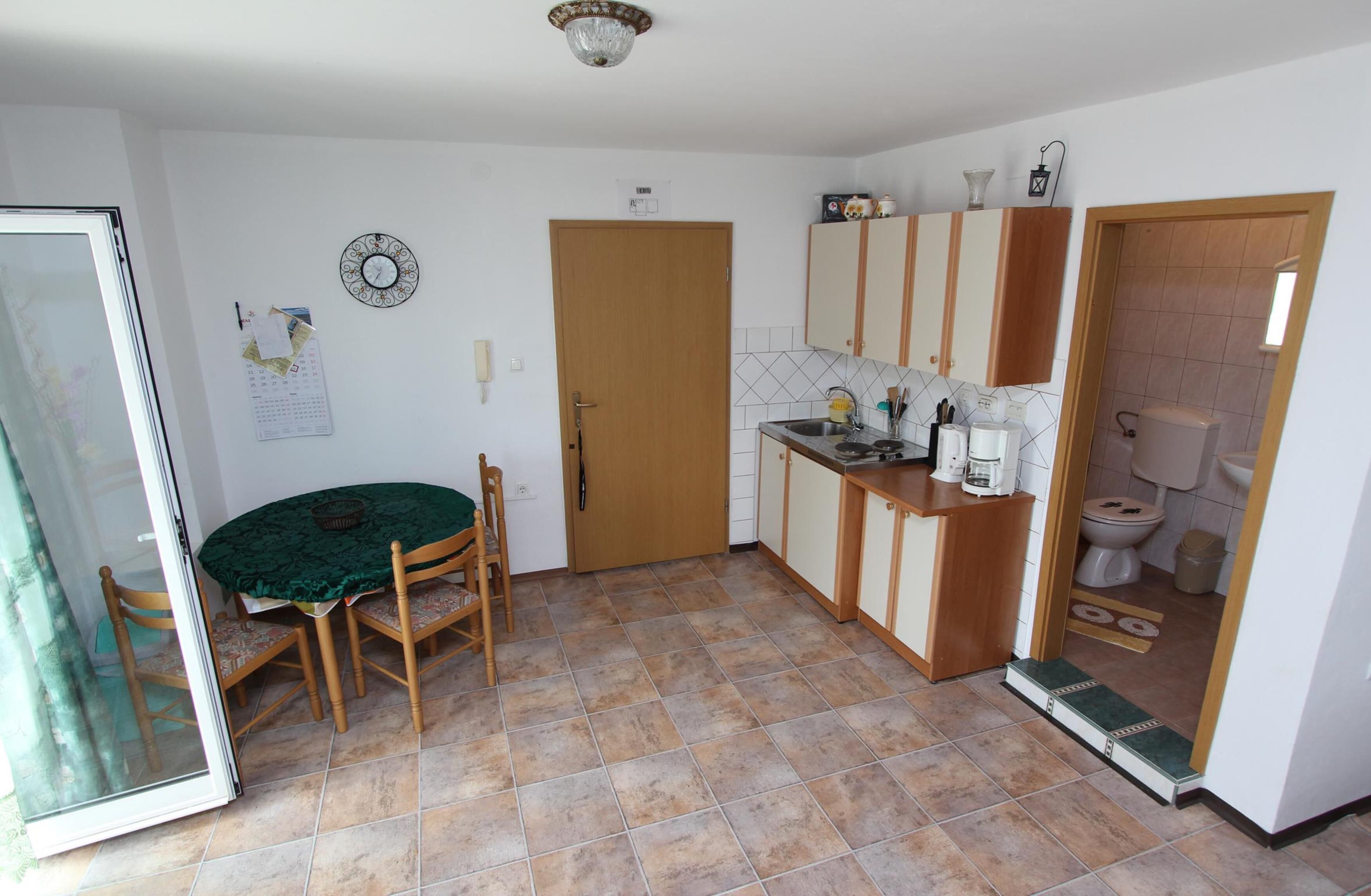 Una cocina compacta con comedor, armarios de madera, un lavamanos y un inodoro visible a través de una puerta abierta.