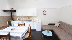 Ett kompakt kök med vita skåp, ett matbord med stolar, ett litet kylskåp och en soffa i ett mysigt vardagsrum.