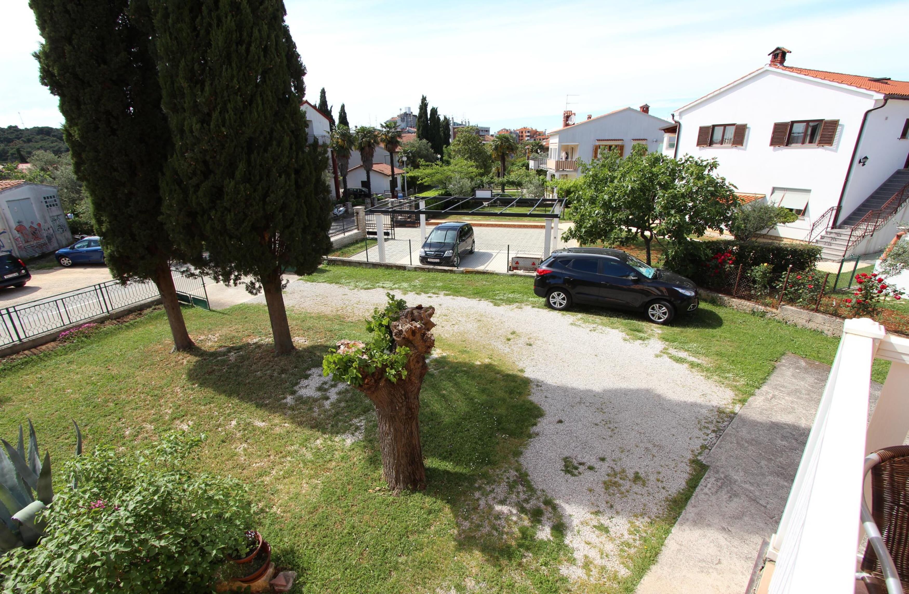 A residential area with a paved driveway, parked cars, and a white house with a red roof.