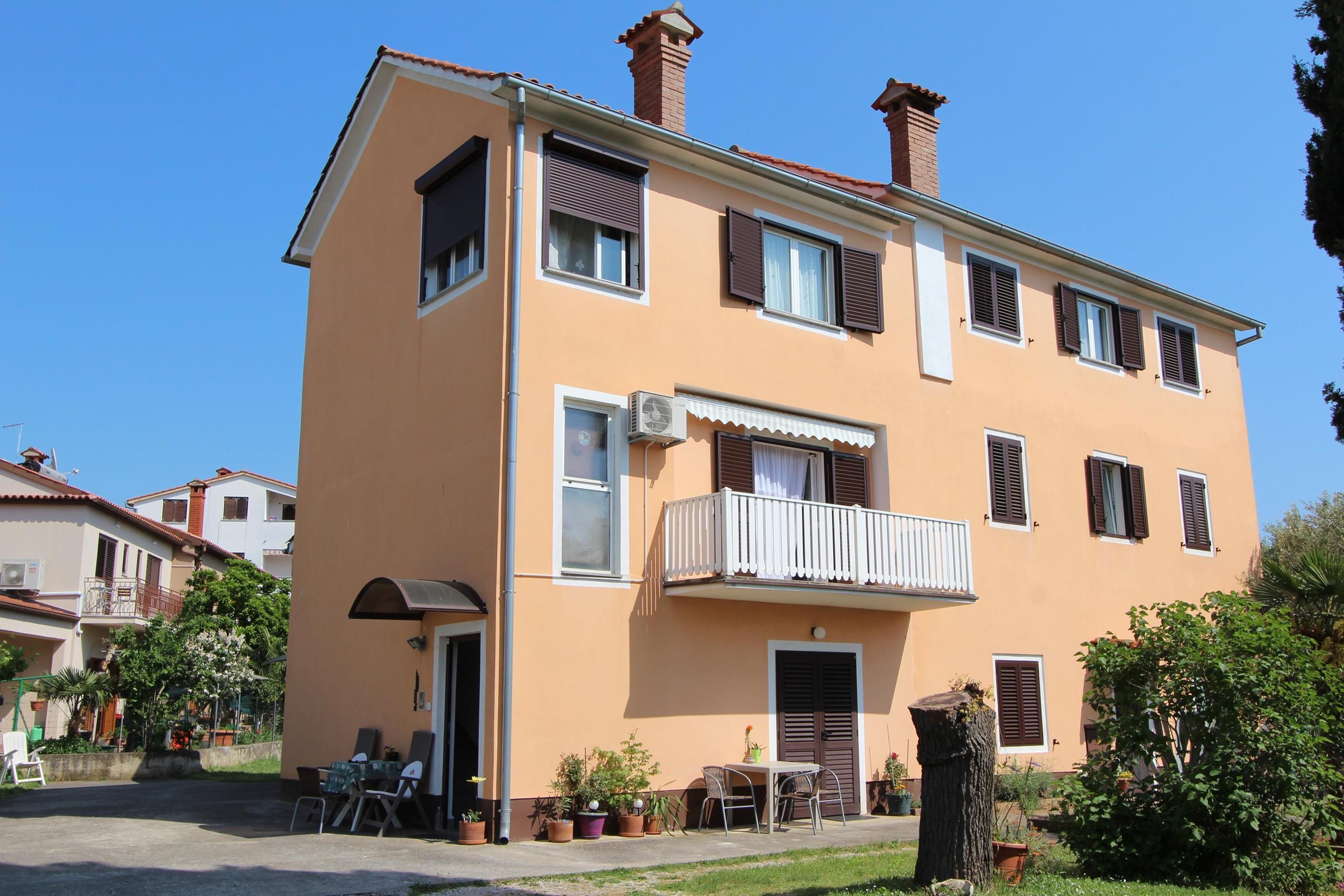 A two-story building with a balcony, a door, and a small outdoor seating area with tables and chairs.