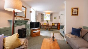 A cozy living room with a television, a wooden coffee table, a sofa, and a dining area with a table and chairs. - Providence House - Four Bedroom Cottage, Sleeps 8 (Saint Breward)