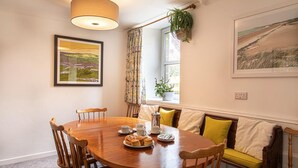 A dining area with a wooden table, chairs, a bench with yellow cushions, a hanging plant, and framed artwork on the walls. - Providence House - Four Bedroom Cottage, Sleeps 8 (Saint Breward)