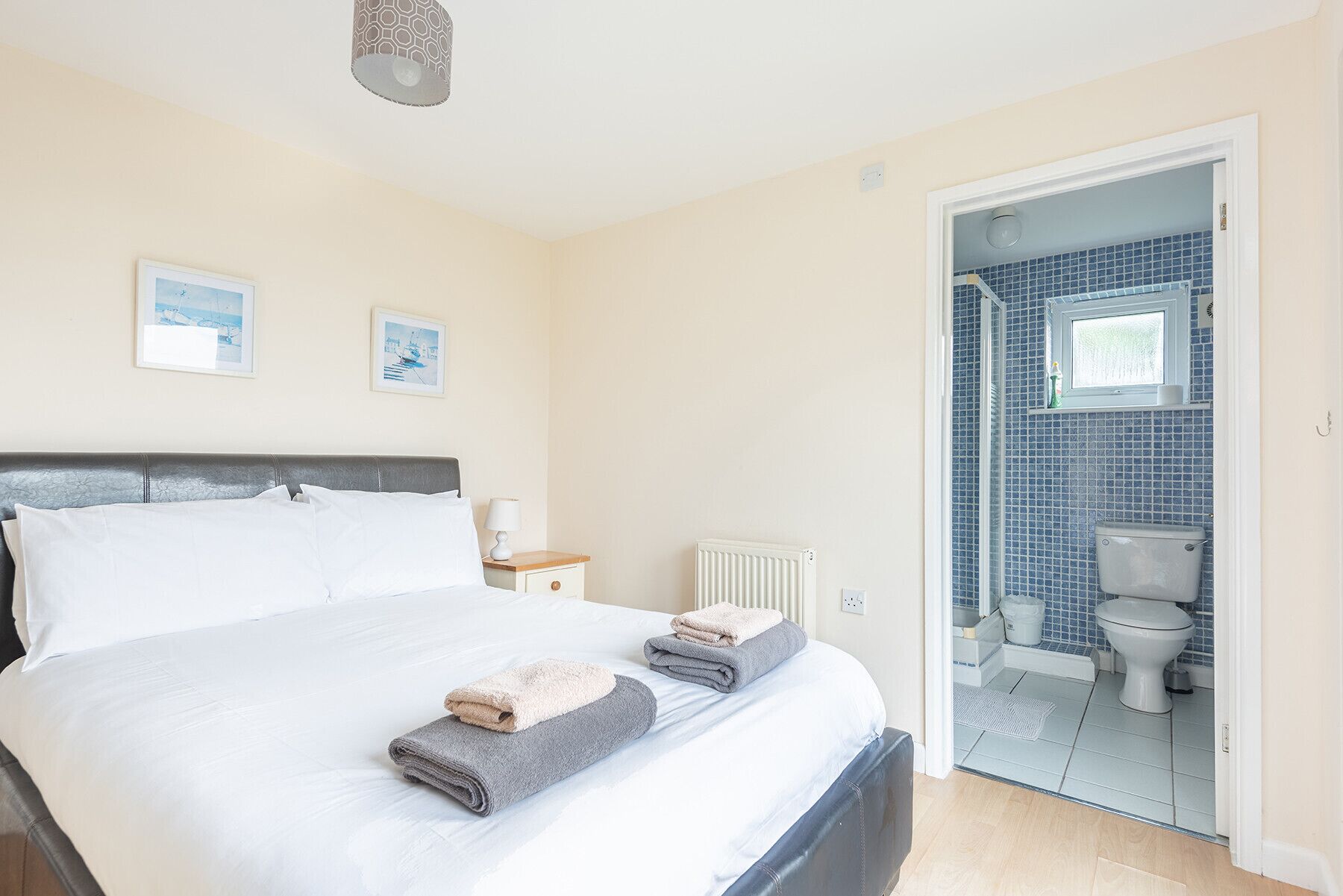A bedroom with a bed, two bedside tables, a radiator, and a bathroom visible through an open door.