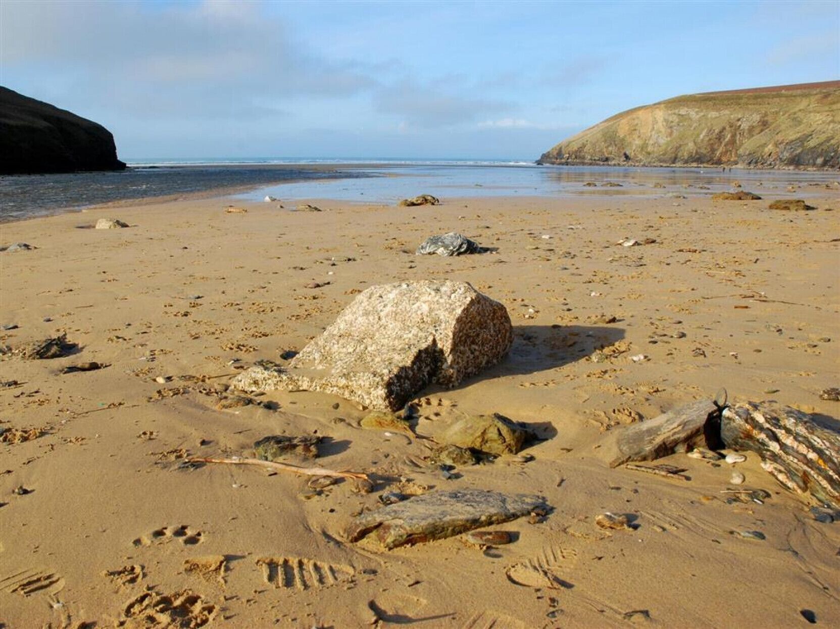 A sandy beach with scattered rocks and footprints.
