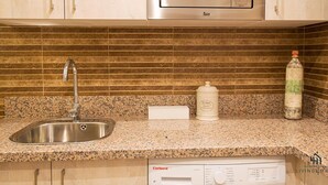 A kitchen with a stainless steel sink, a microwave, a Corby dishwasher, and a tiled backsplash. - Mariblanca Bajo B Deluxe Living4malaga (Málaga)