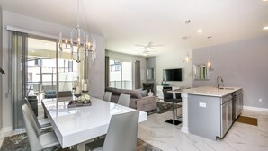 A modern kitchen with a central island, a dining area with a large table and chairs, and a living area with a sofa and TV. - Champions Gate Exec Villas- 1571sand (Davenport)