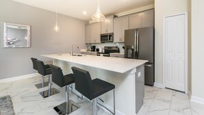 A modern kitchen with a central island, bar stools, stainless steel appliances, and pendant lighting. - Champions Gate Exec Villas- 1571sand (Davenport)