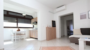 A modern apartment with a kitchen, dining area, and living room. It features a tiled floor, a wooden cabinet, and a sofa. - Apartments Rozi (Rovinj)