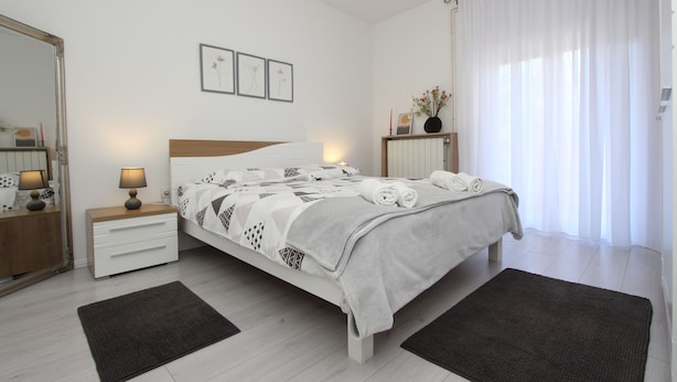 A modern bedroom with a bed, bedside tables, a mirror, and a window with curtains. - Apartments Rozi (Rovinj)